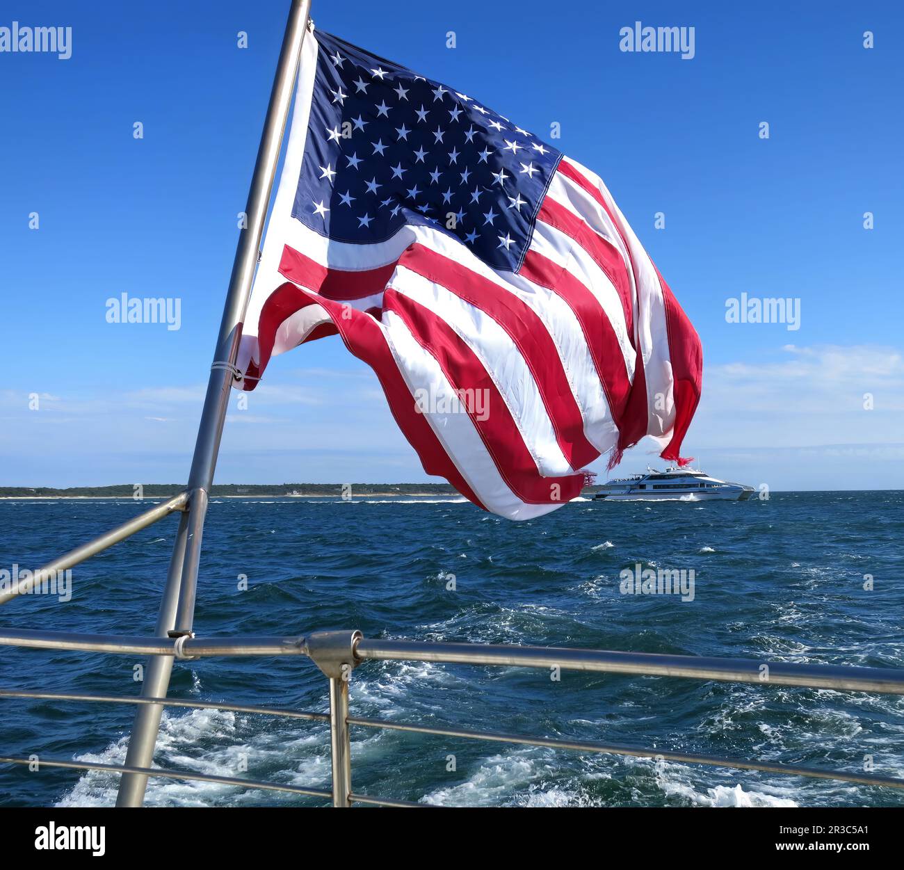 American Flag off the back of a boat and a yacht the the background in Hyannis Harbor on Cape Cod, Massachusetts USA. A good look for the 4th of July. Stock Photo