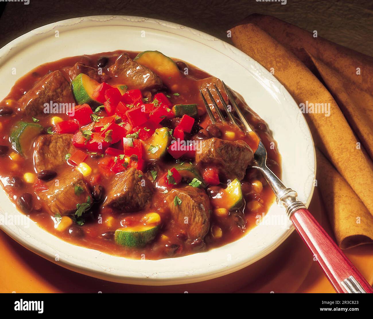 A bowl of Mexican style beef stew with a fork and golden napkin Stock Photo