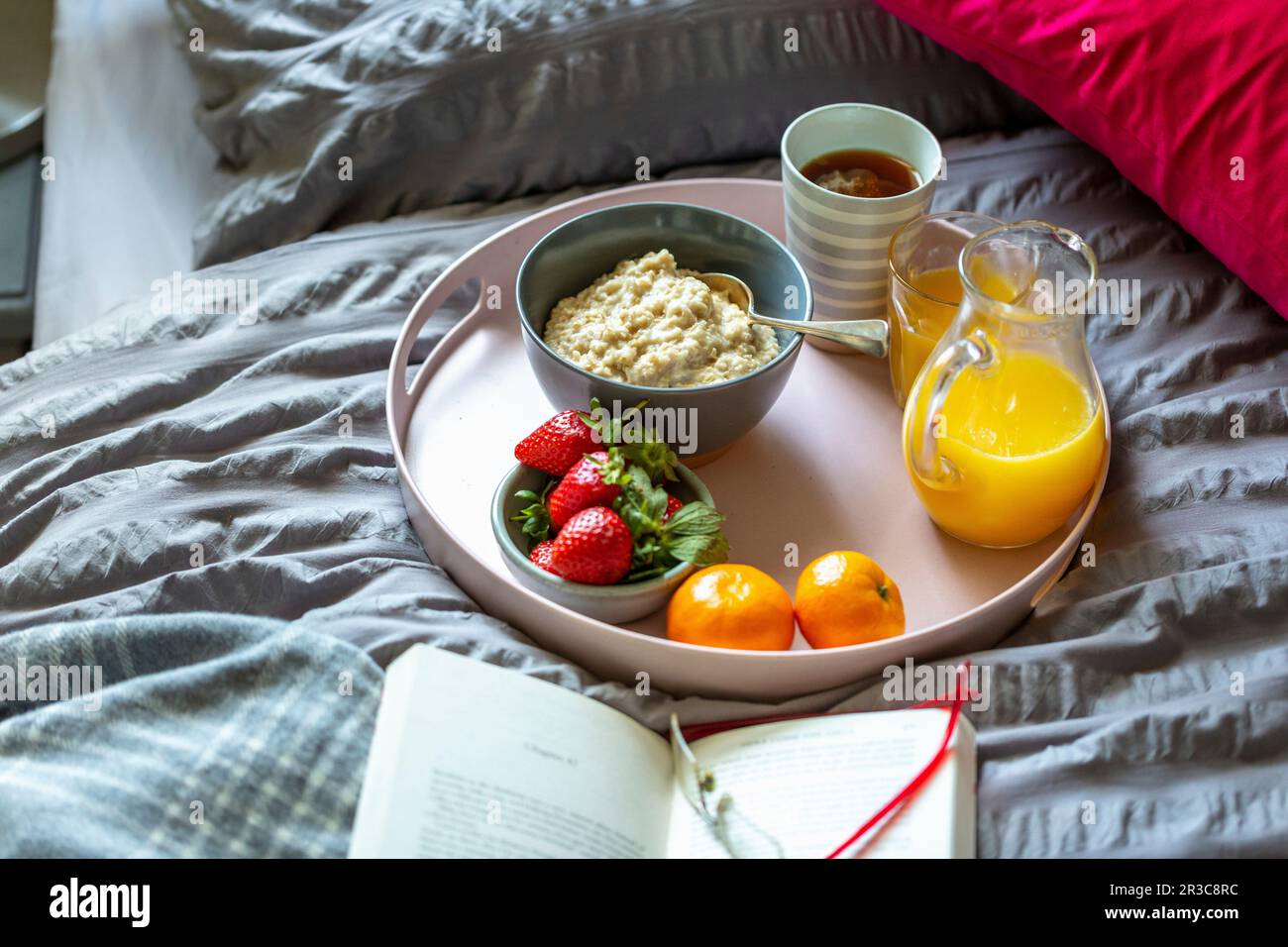 Breakfast tray with porridge, tea, orange juice and fruit on a bed