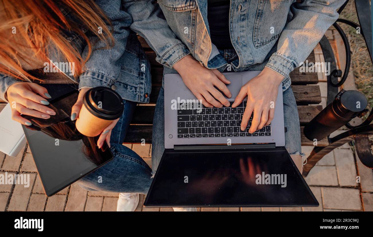 Close-up of the hands of a man and a woman with a laptop and tablet while working using laptop, sitting on the bench in park Stock Photo