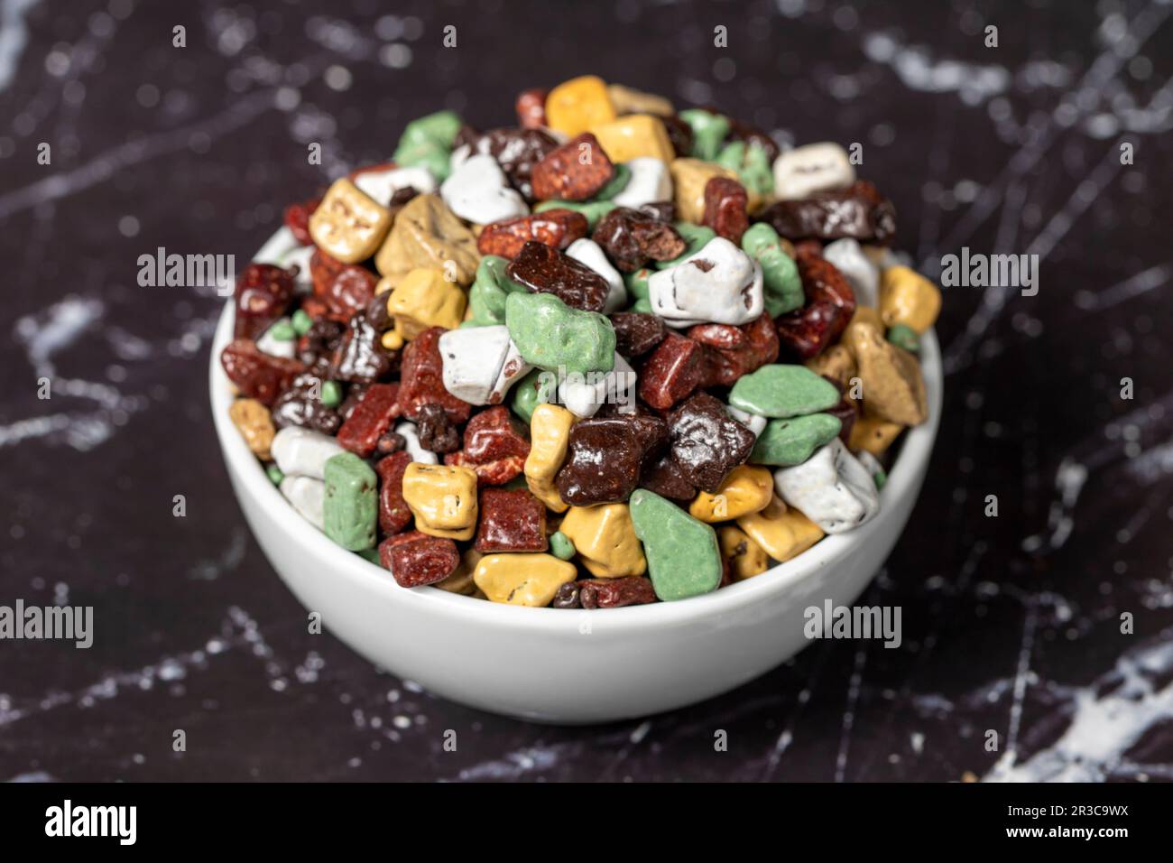 Colorful chocolate candy stones. Stone chocolate dragee in ceramic bowl on dark background. Small multi-colored candies. Close up Stock Photo