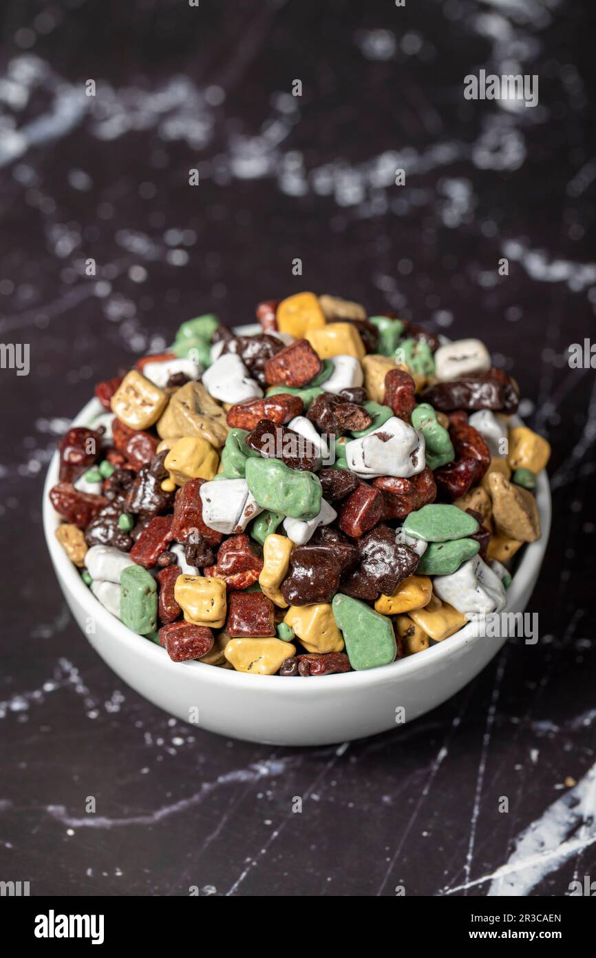 Colorful chocolate candy stones. Stone chocolate dragee in ceramic bowl on dark background. Small multi-colored candies. Close up Stock Photo