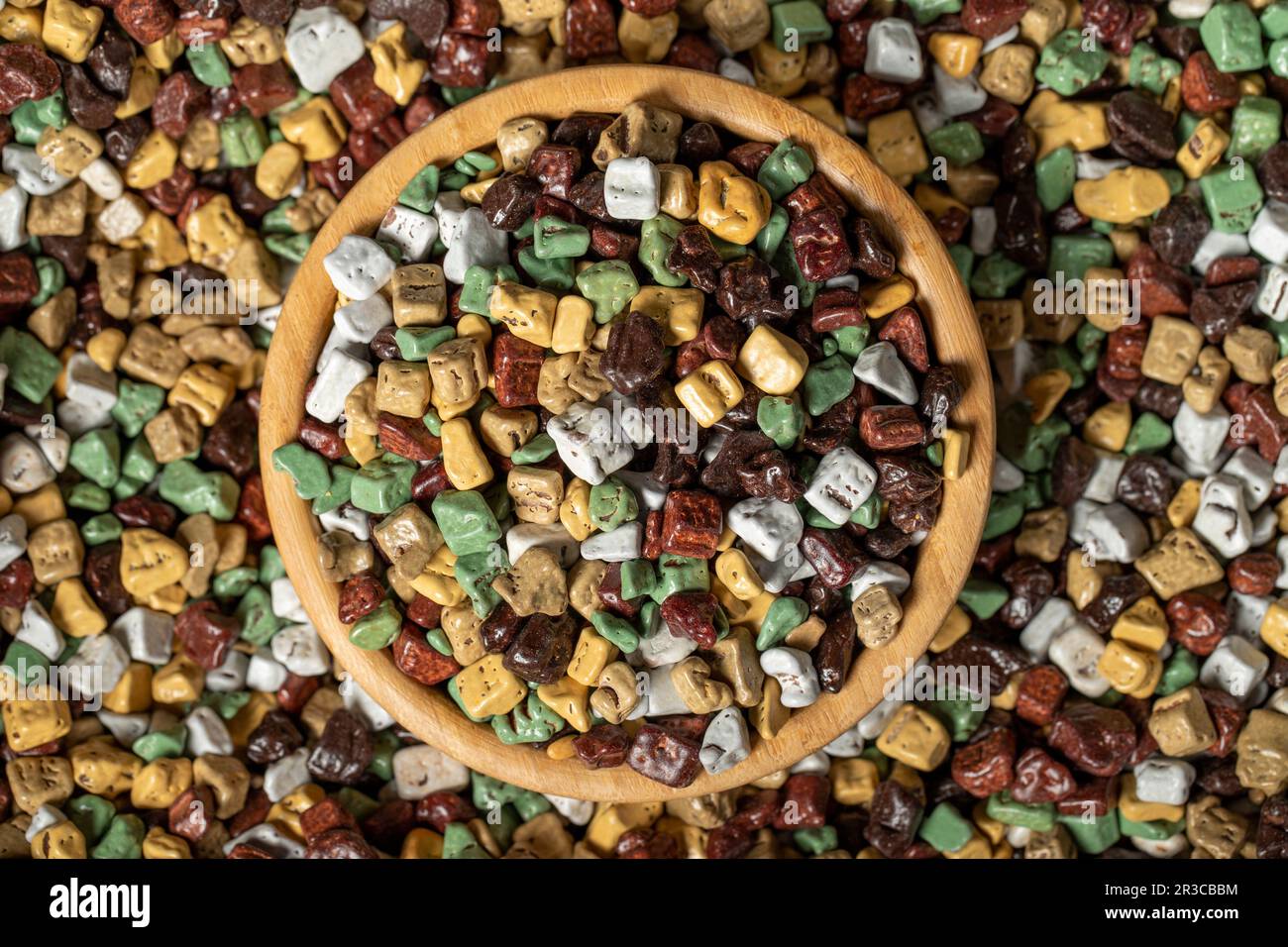 Colorful chocolate candy stones. Stone chocolate dragee in wooden bowl. Small multi-colored candies. Top view Stock Photo