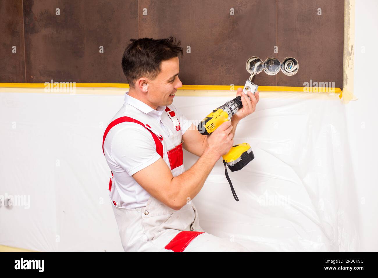 The electrician with a drill fastens the socket Stock Photo