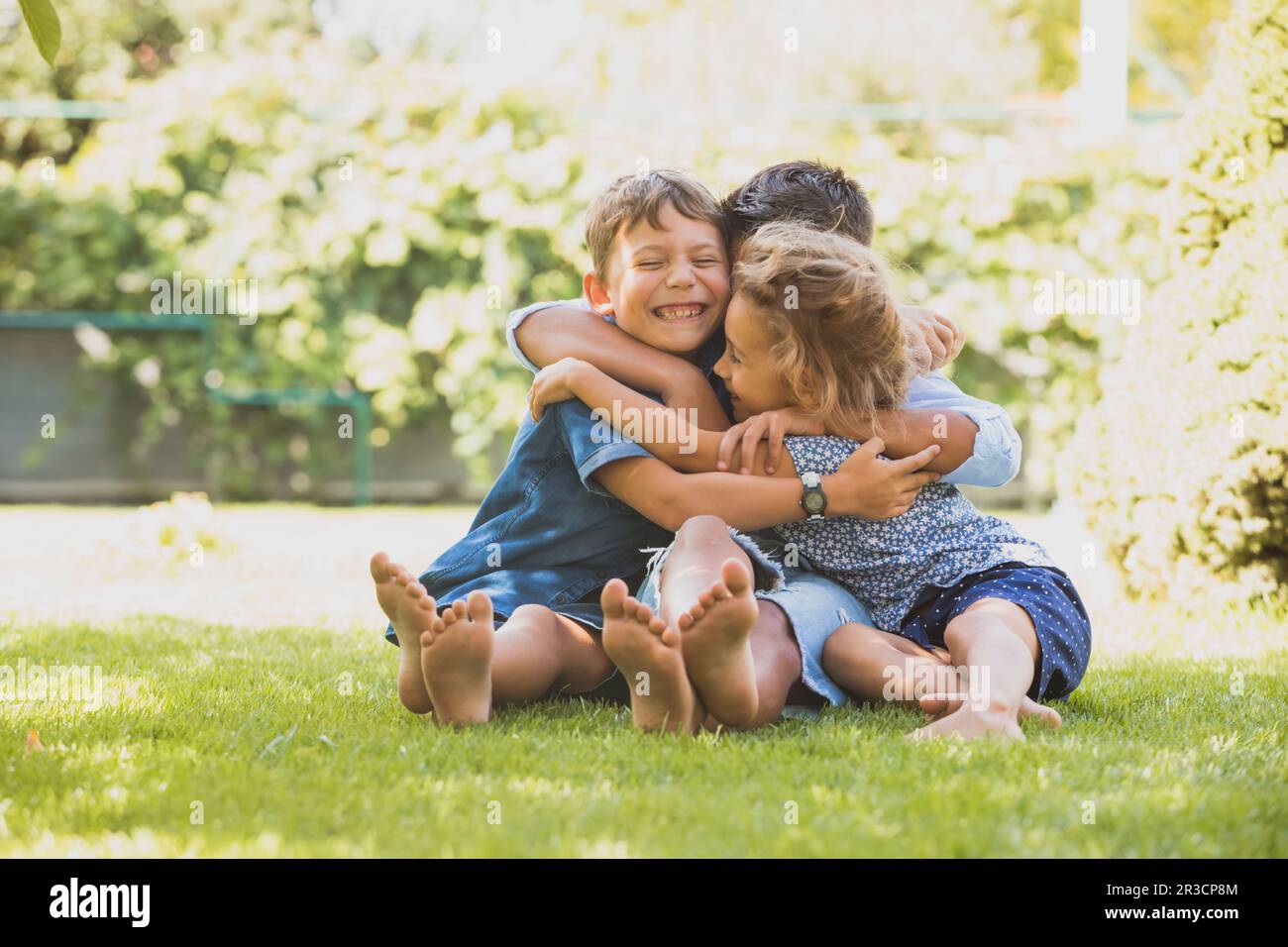 Three little kids are hugging together outdoors Stock Photo