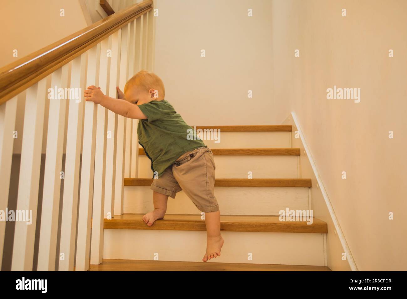 Adorable toddler boy slowly walking down the stairs, holding railings
