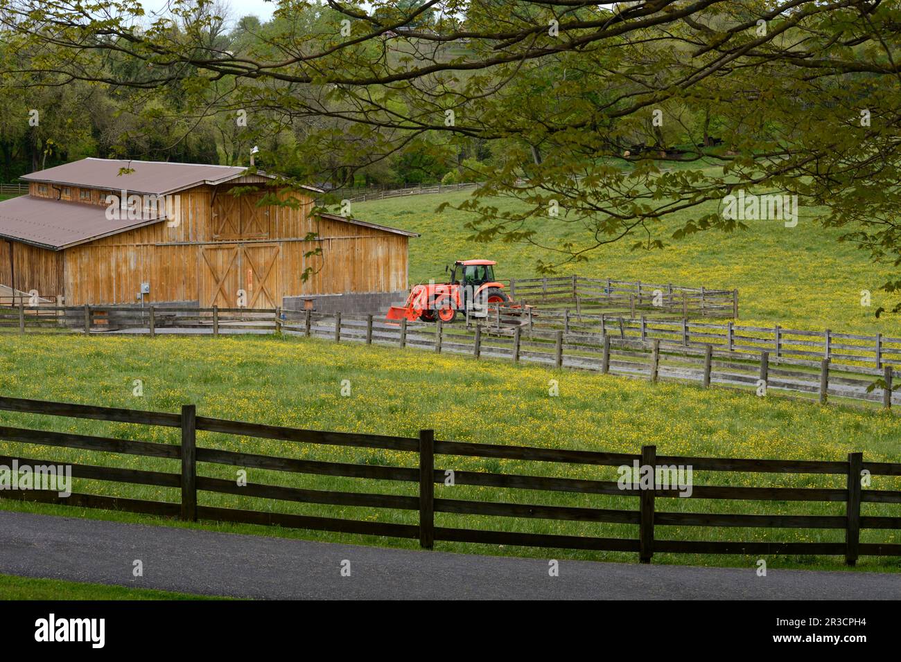 A red Kubota tractor is parked beside a cattle barn on a farm in