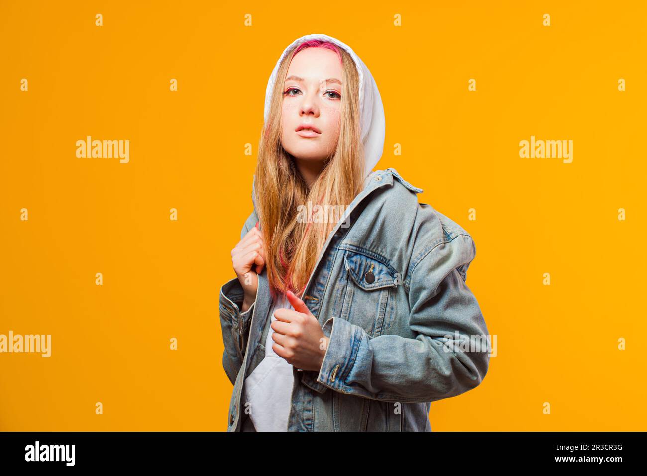Cool young woman posing in jeans jacket on yellow background Stock Photo
