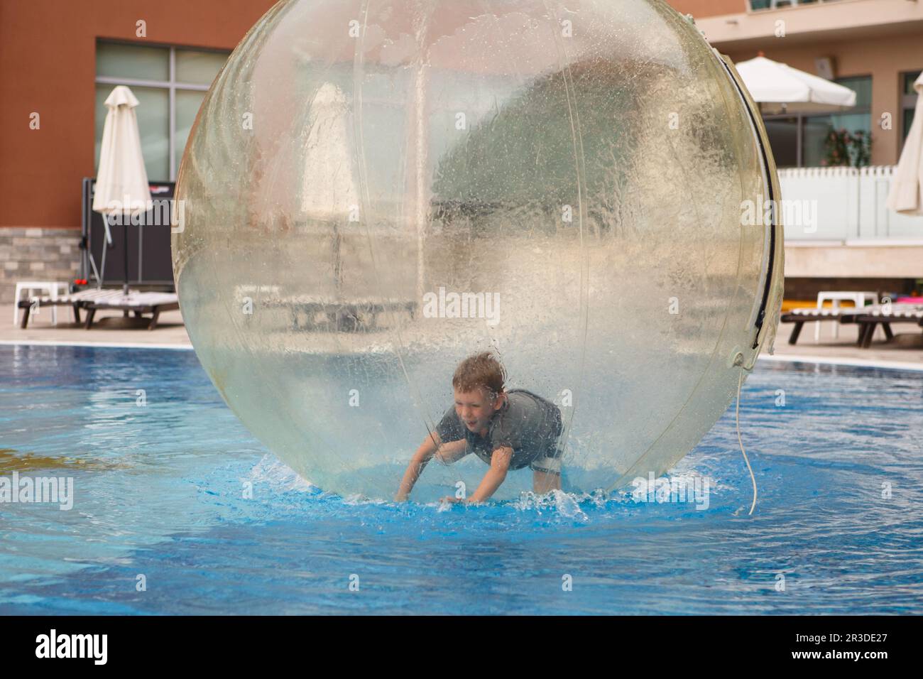 Child have fun inside big plastic balloon on the water of swimming pool on the summer resort. Little Stock Photo