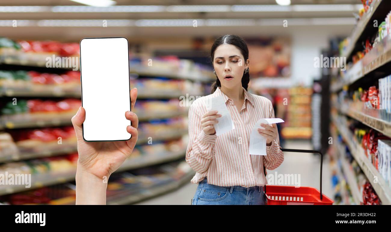 Sales in supermarket. Portrait of young Caucasian shocked woman check paper receipts. Hand shows smartphone with white screen mock up. Concept of disc Stock Photo