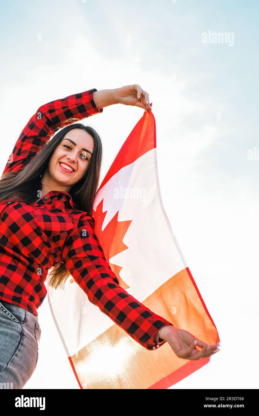 Young millennial brunette woman holding The National Flag of Canada. Canadian Flag or the Maple Leaf. Tourist traveler or patrio Stock Photo