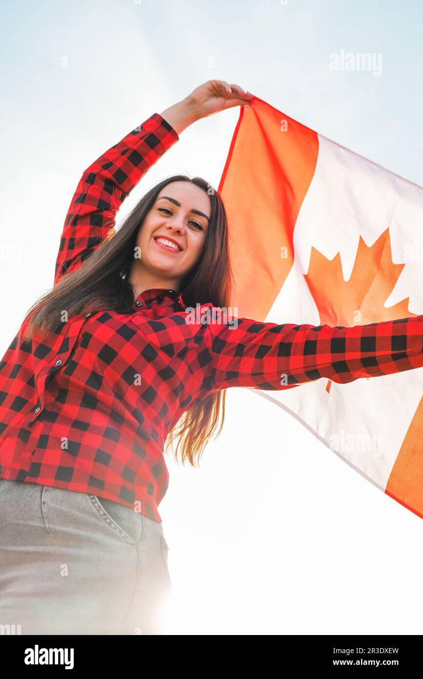 Young millennial brunette woman holding The National Flag of Canada. Canadian Flag or the Maple Leaf. Tourist traveler or patrio Stock Photo