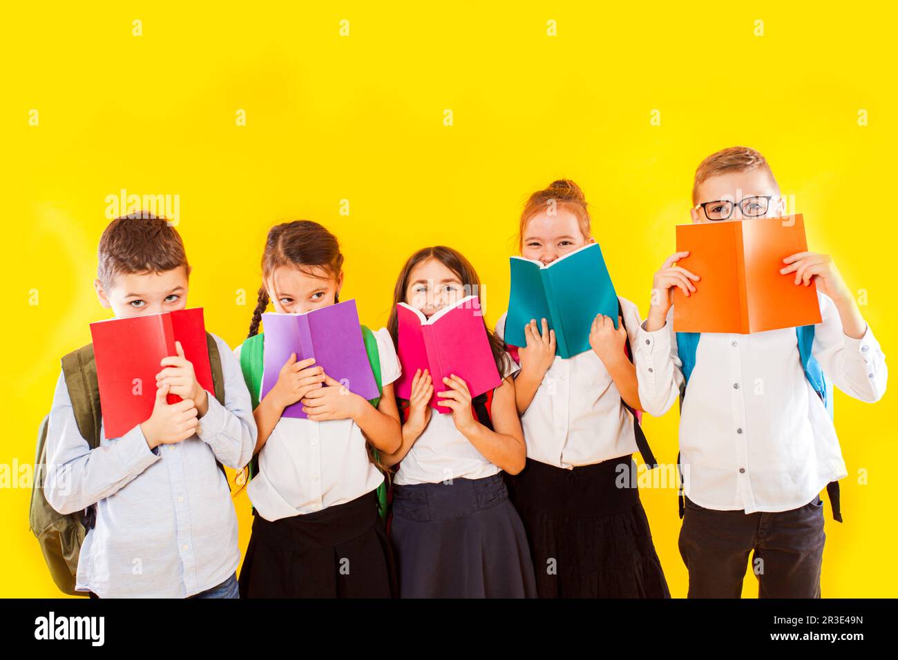 Happy schoolkids standing with colorful books isolated on yellow background. Kids hiding face behind books Stock Photo
