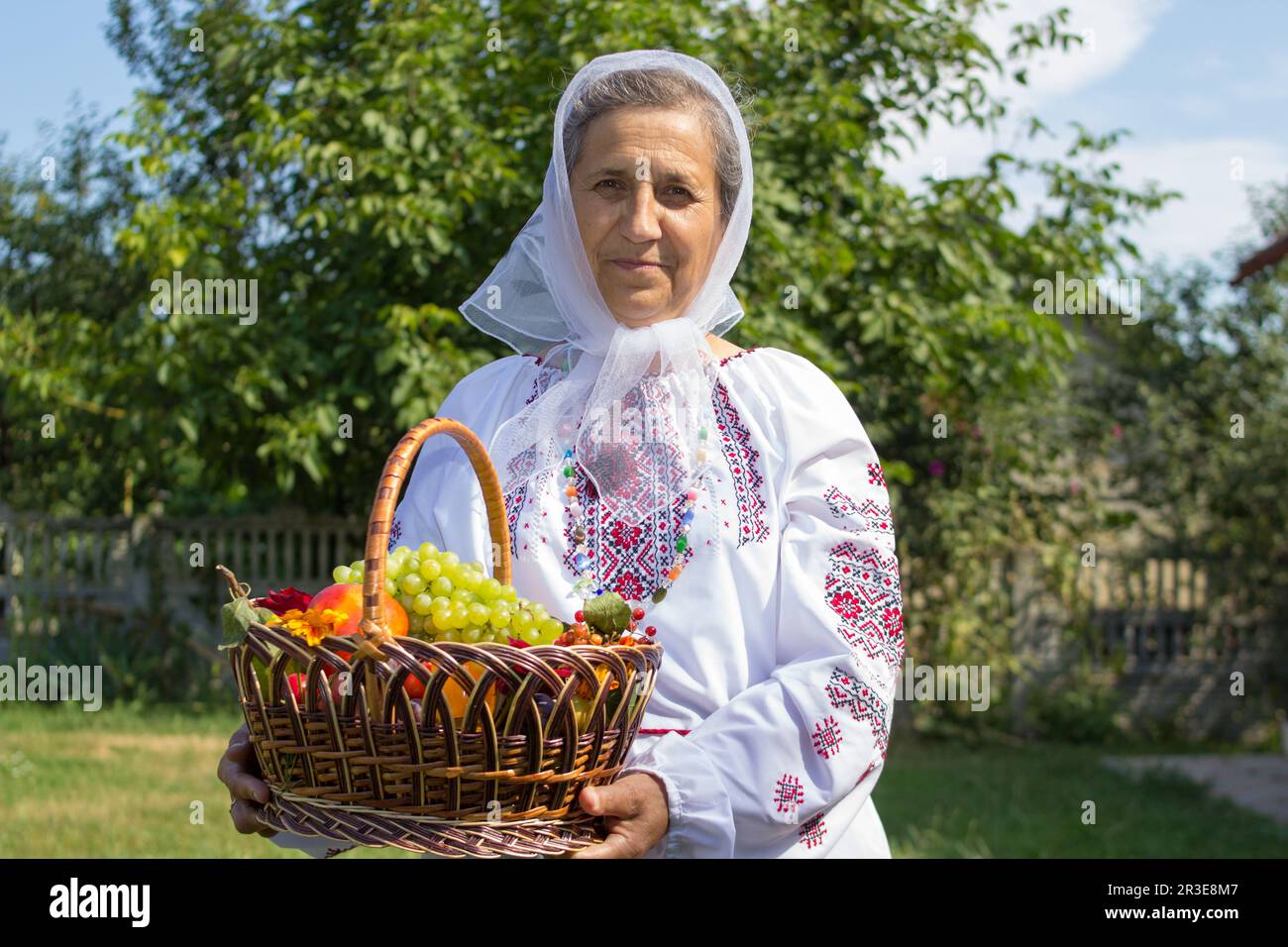 grandmother holds a full basket of fruits in an embroidered blouse Stock Photo