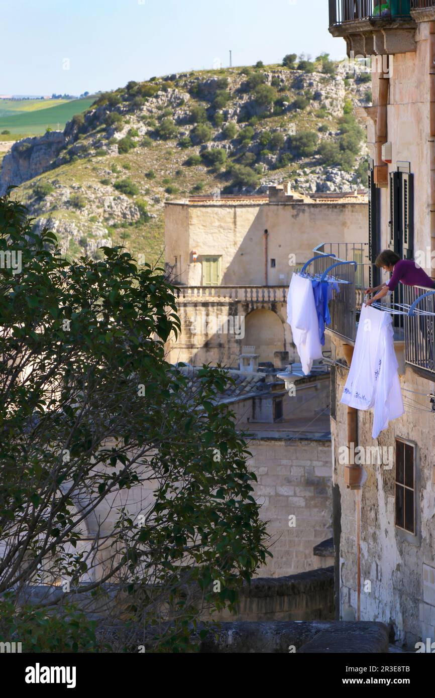 Moments in local daily life in the historic Sassi of Matera, Basilicata region of Italy. Woman hanging the clothes to dry on balcony. Stock Photo