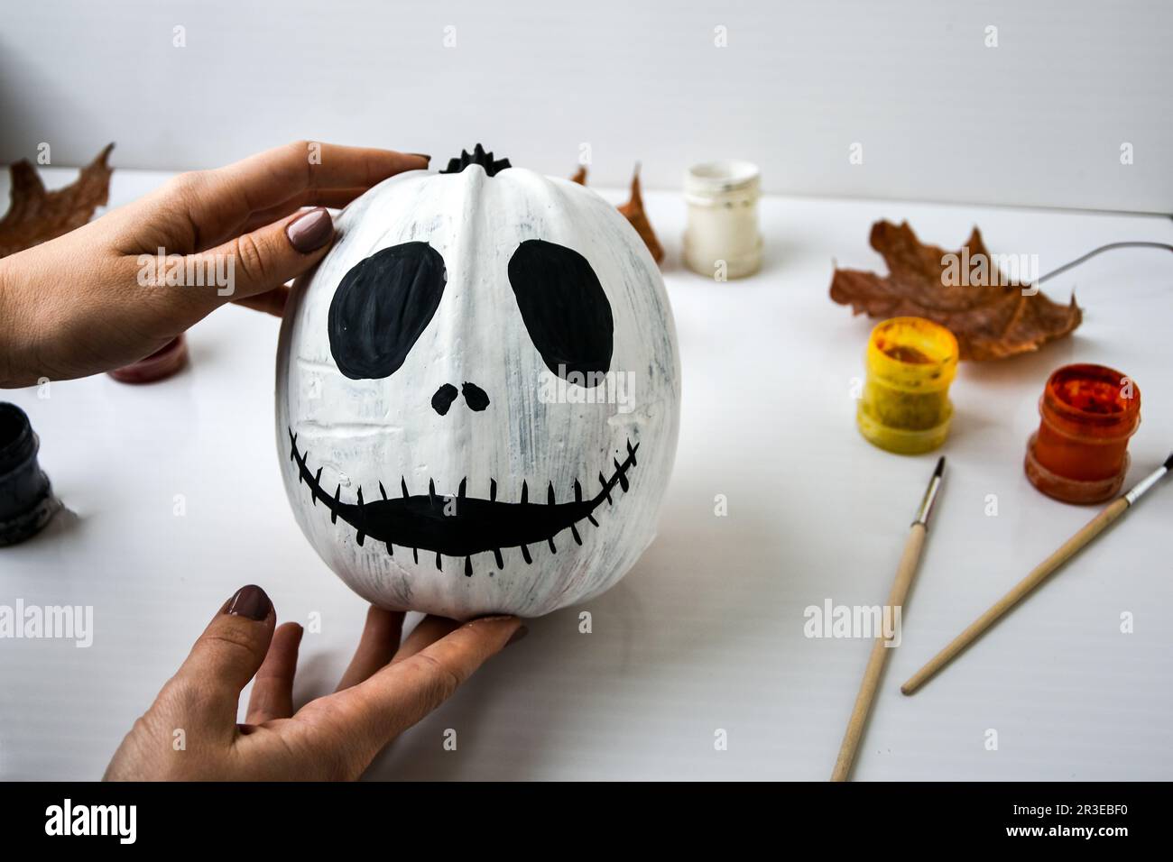 Woman paints face on orange pumpkin for Halloween. Autumn leaves. Diy children craft. Do it yourself. Stock Photo
