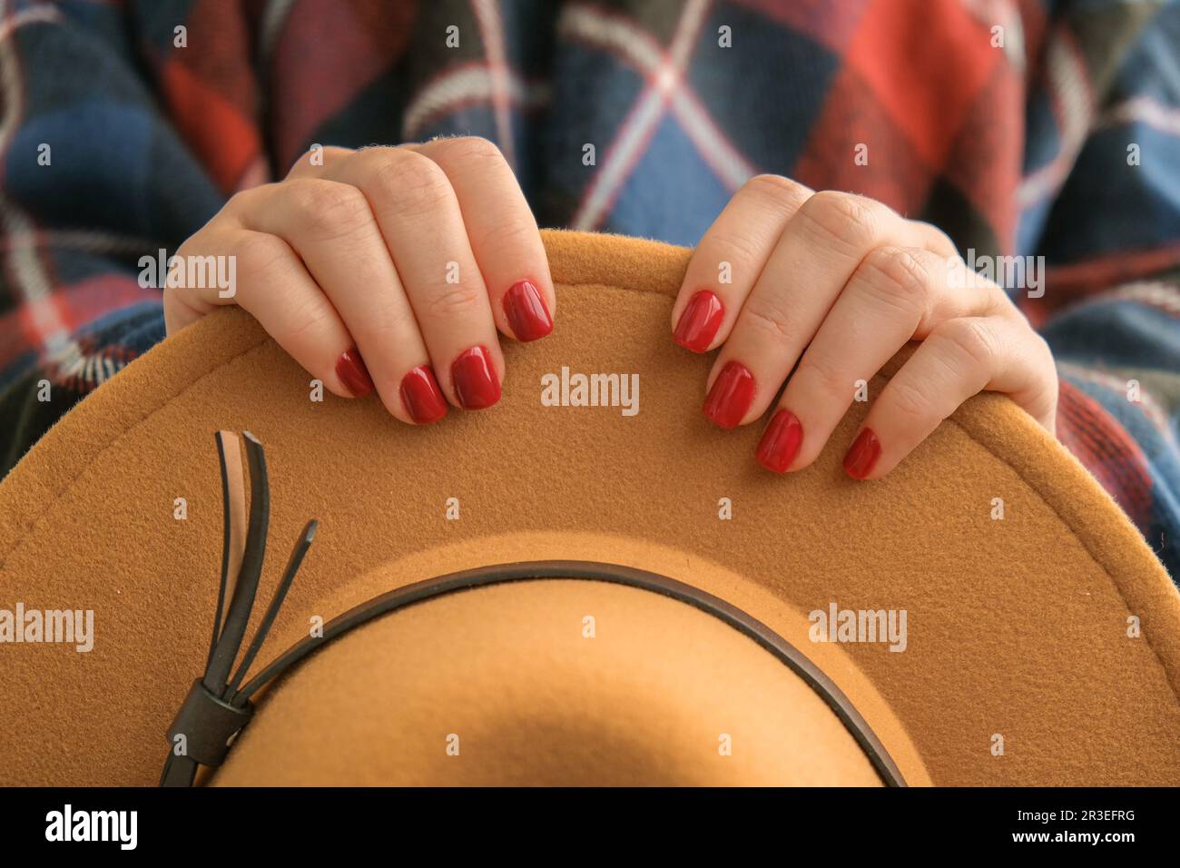 Stylish red female nails. Woman in poncho holding brown trendy hat. Modern Beautiful manicure. Autumn winter nail design concept Stock Photo