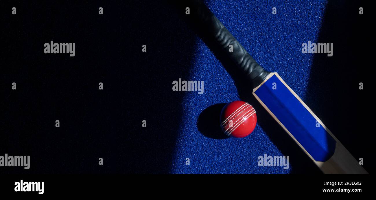 Cricket bat and red ball with natural lighting on blue background ...