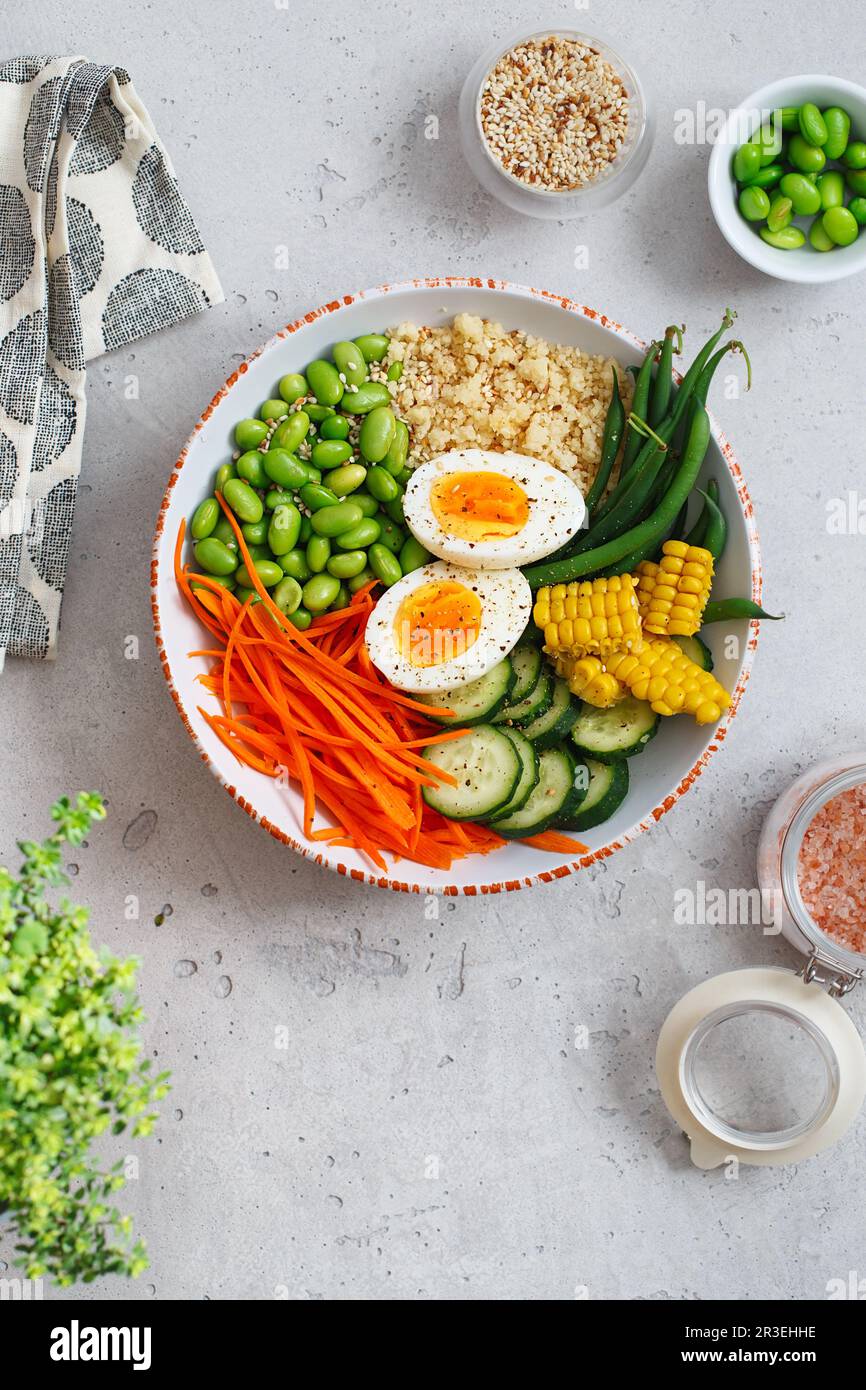 Healthy salad with couscous, carrots, cucumber, green beans, soybeans, corn and an egg on a gray concrete background. Food and h Stock Photo