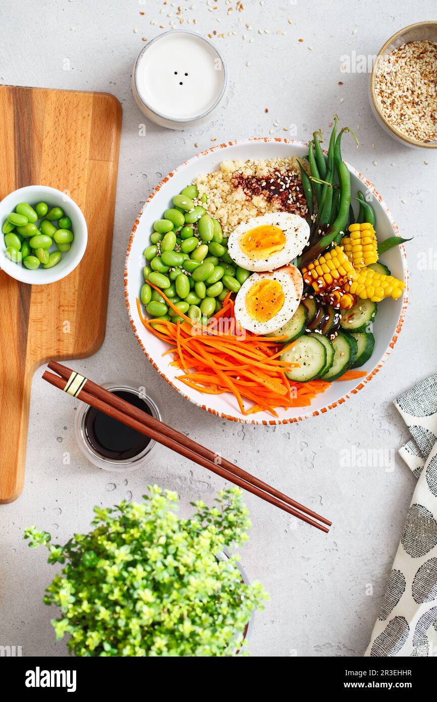 Healthy salad with couscous, carrots, cucumber, green beans, soybeans, corn and an egg on a gray concrete background. Food and h Stock Photo