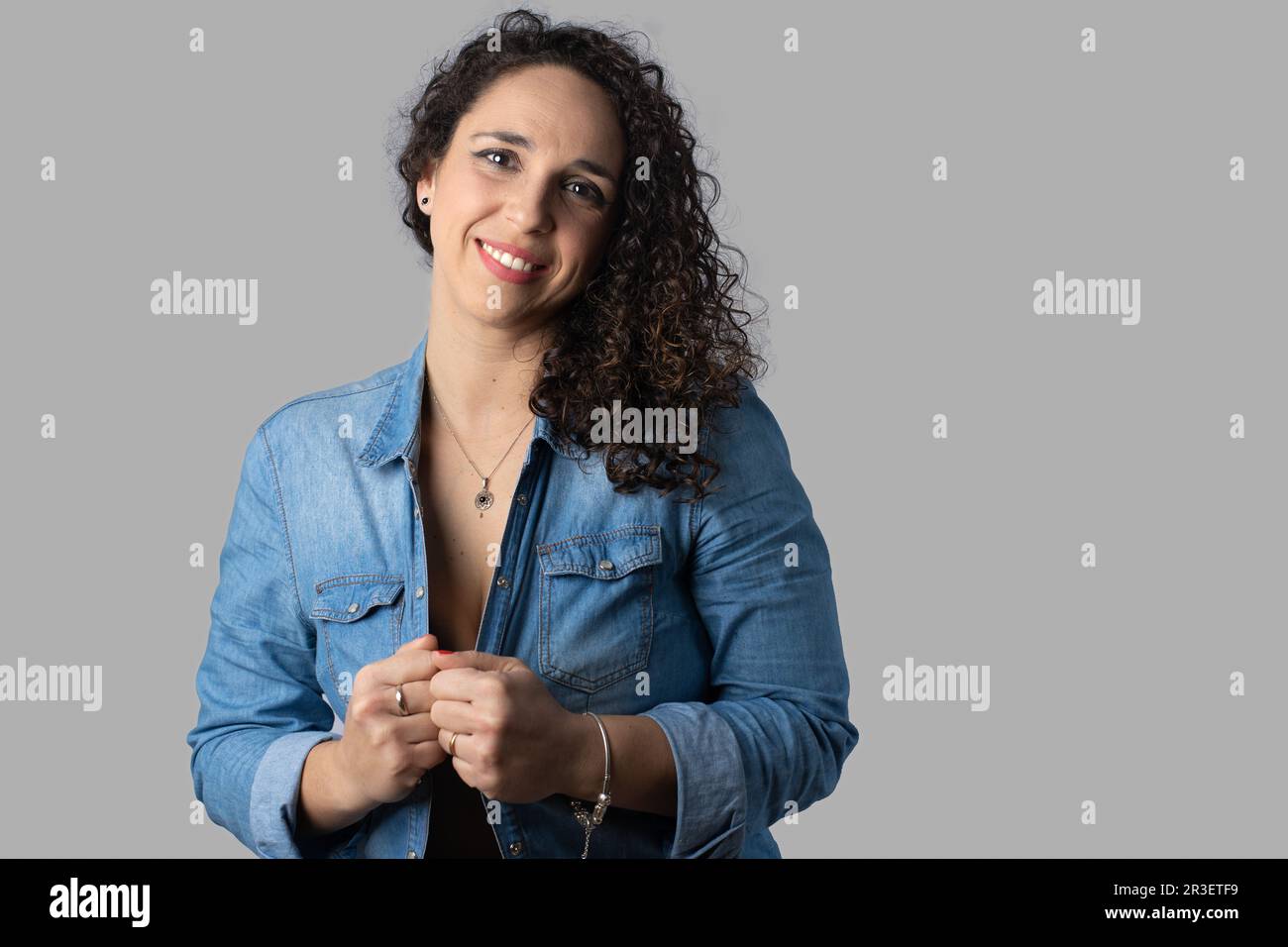 Young woman with curly black hair wearing blue denim shirt and hands grasping shirt Stock Photo