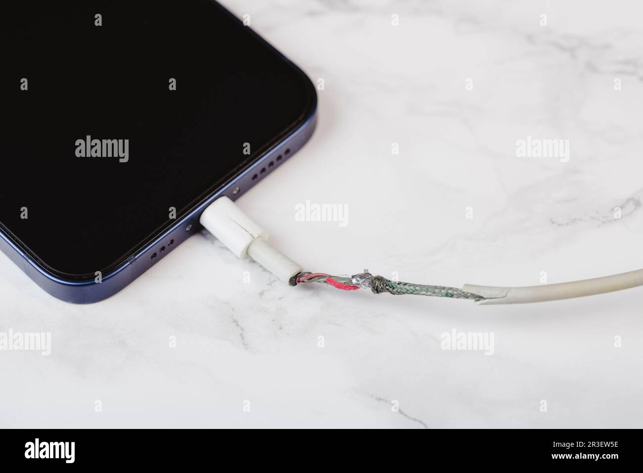 Top view of broken phone charger cable on the white table, visible wires Stock Photo