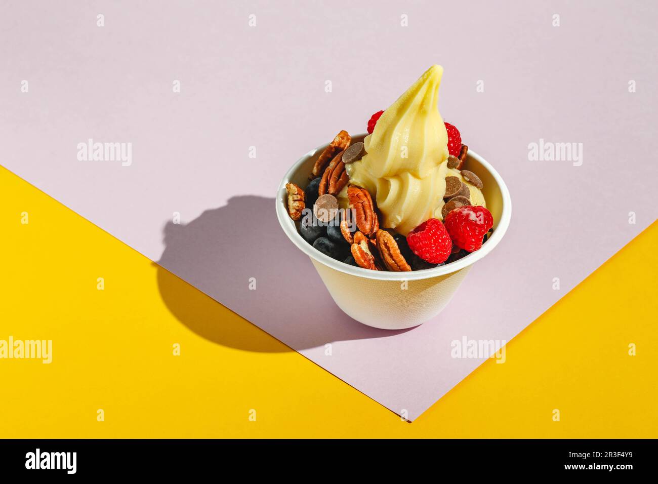 Frozen yogurt with raspberries, blueberries, chocolate drops and pecans. Hard light, deep shadow Stock Photo