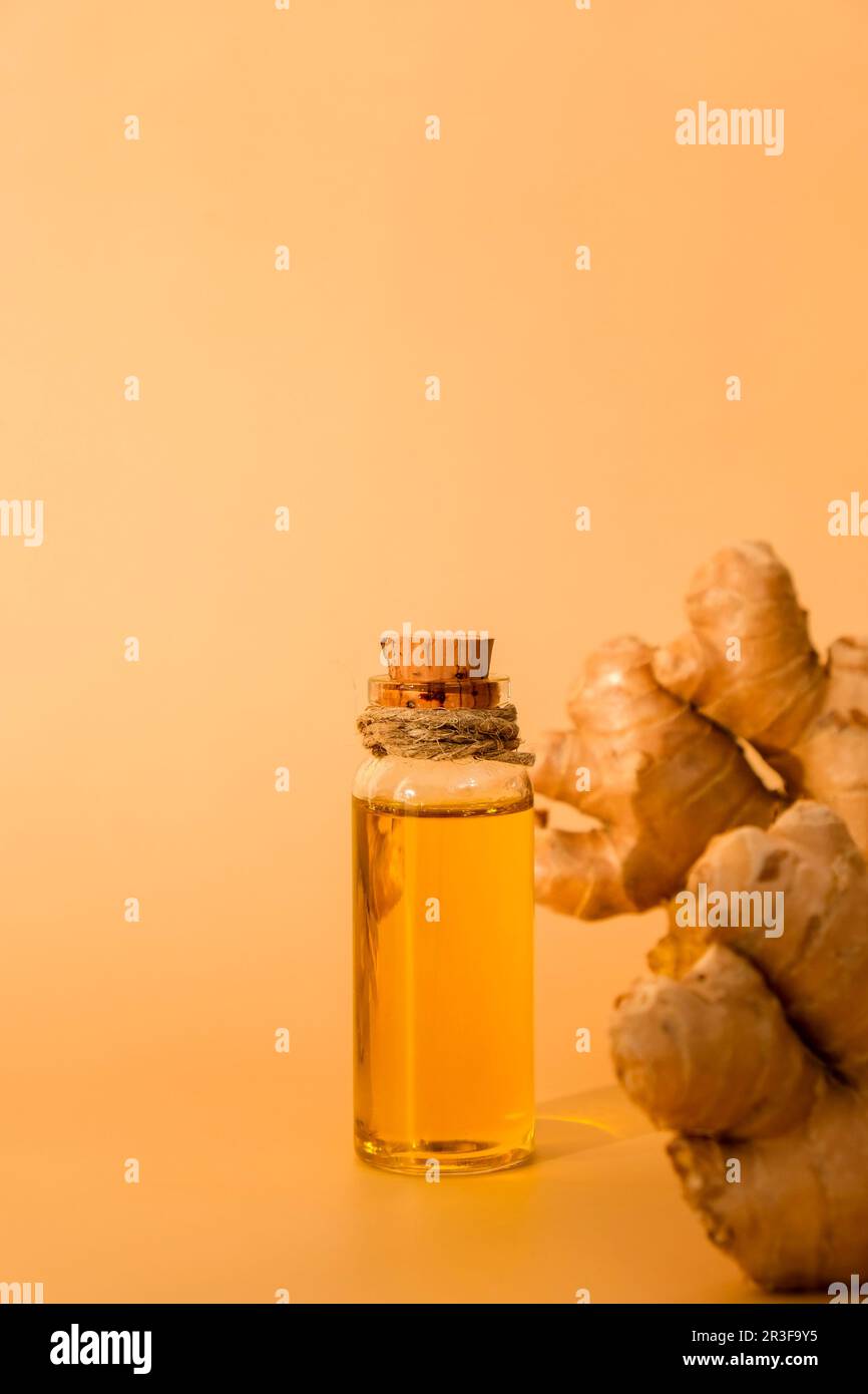 Glass bottle of essential ginger oil, ginger root on beige background