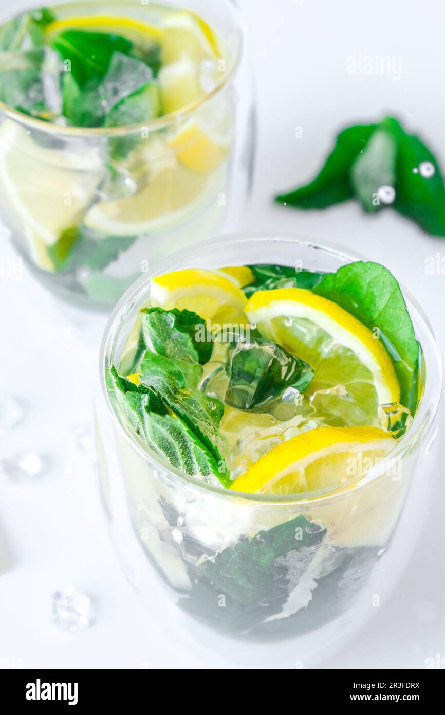 Mojito refreshing cocktail, alcohol drink. Lemonade with lemon and mint leaves on light background. Ice cube fall splash drops. Stock Photo
