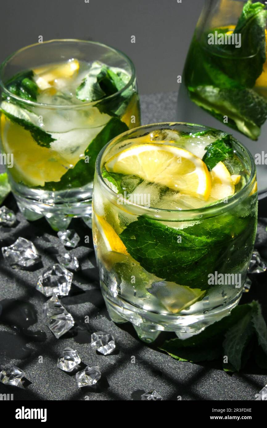 Mojito refreshing cocktail, alcohol drink. Lemonade with lemon and mint leaves on dark background. Trendy shadows Ice cubes. Sum Stock Photo