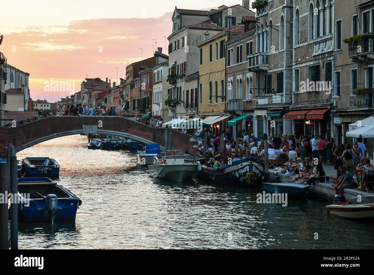 Bridge and Fondamenta dei Ormesini waterfront overlooking Rio della Misericordia canal, crowded with tourists on a summer evening at sunset, Venice Stock Photo