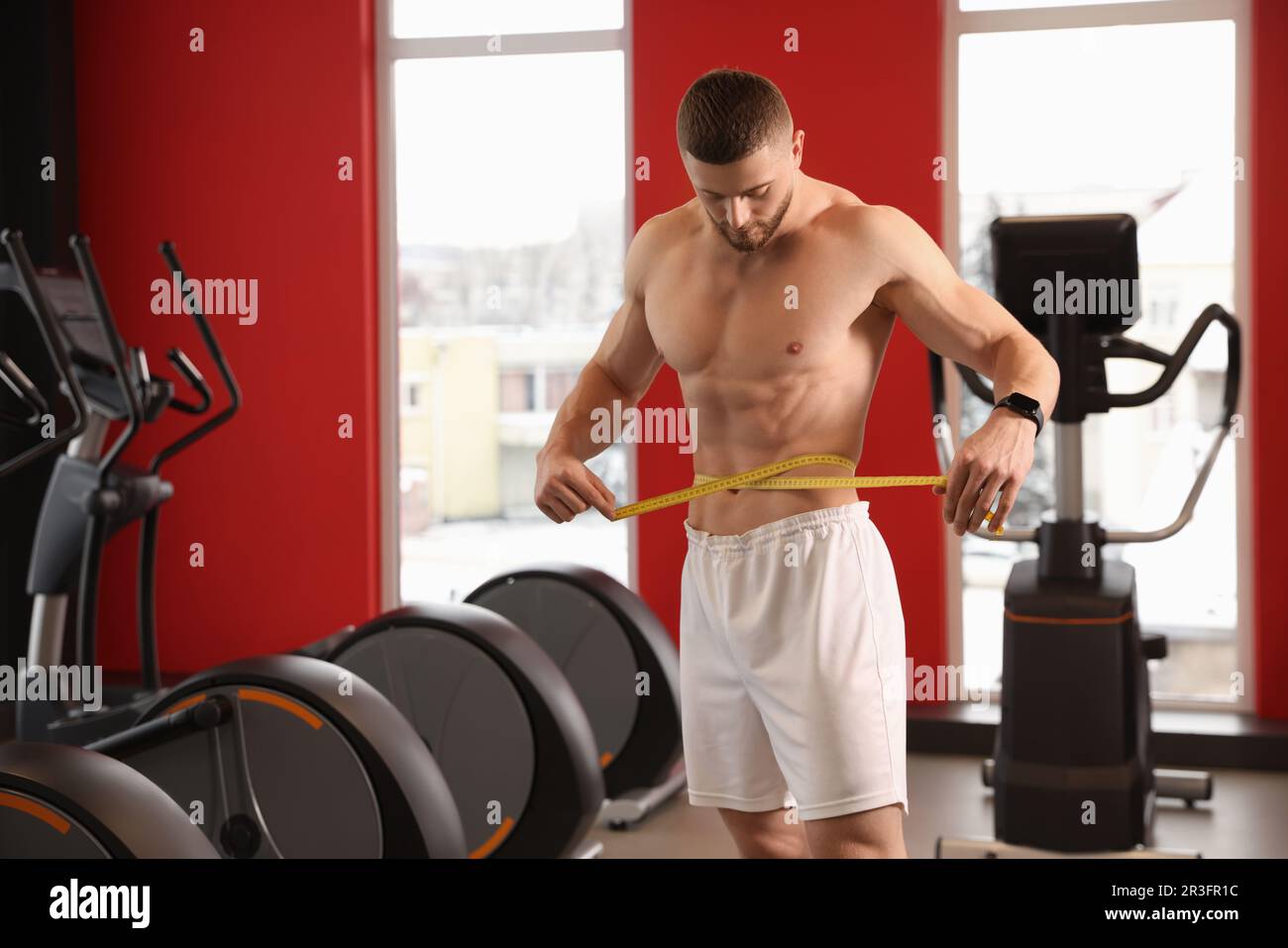 Athletic man measuring waist with tape in gym Stock Photo