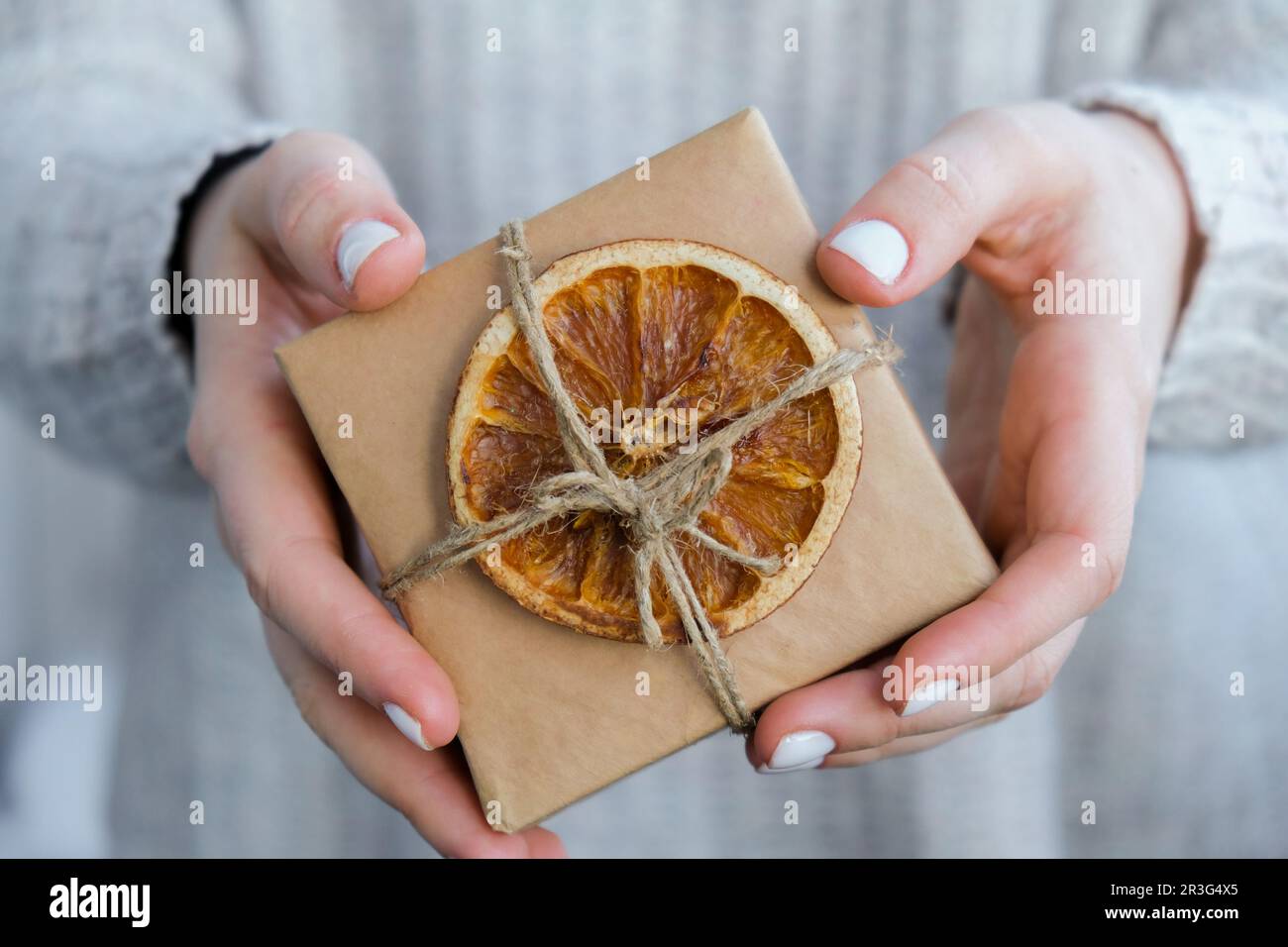 Woman giving Box with New Year's gifts, wrapped in craft paper and decorated with dry orange slices. Holidays and Gifts concept. Stock Photo