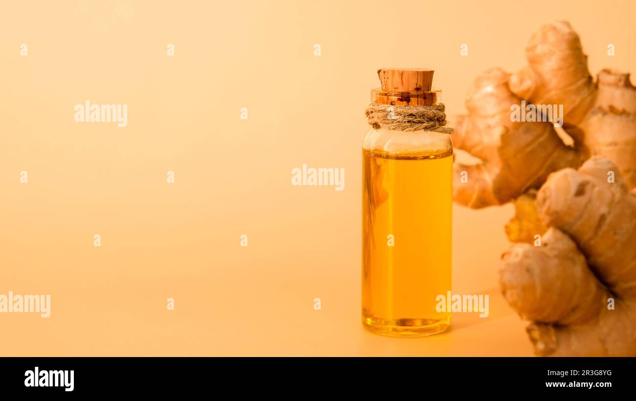 Glass bottle of essential ginger oil, ginger root on beige background