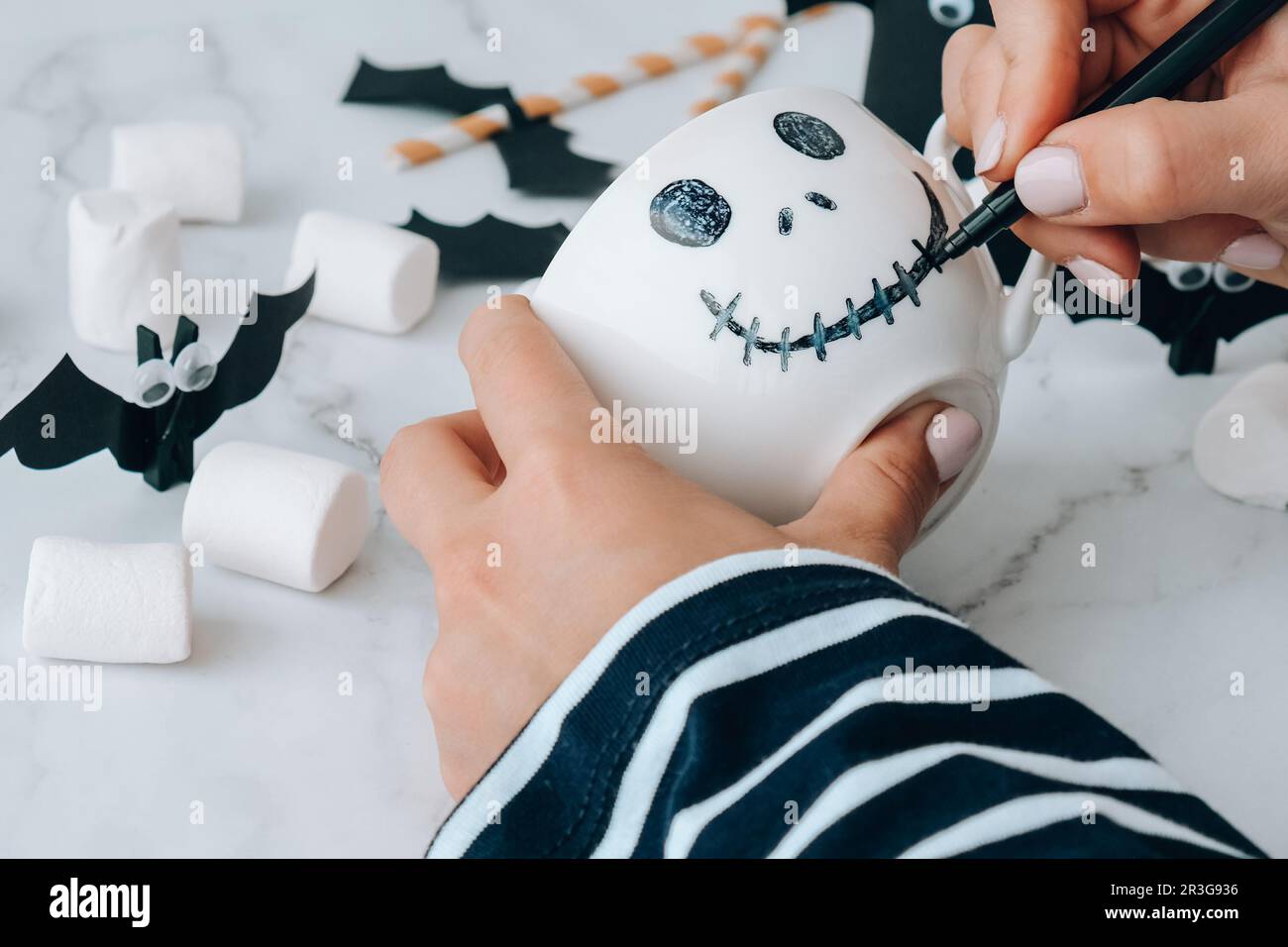 Female hands paint on white cup scary jacks face DIY for kids Halloween home activities Holiday art children craft Handmade deco Stock Photo