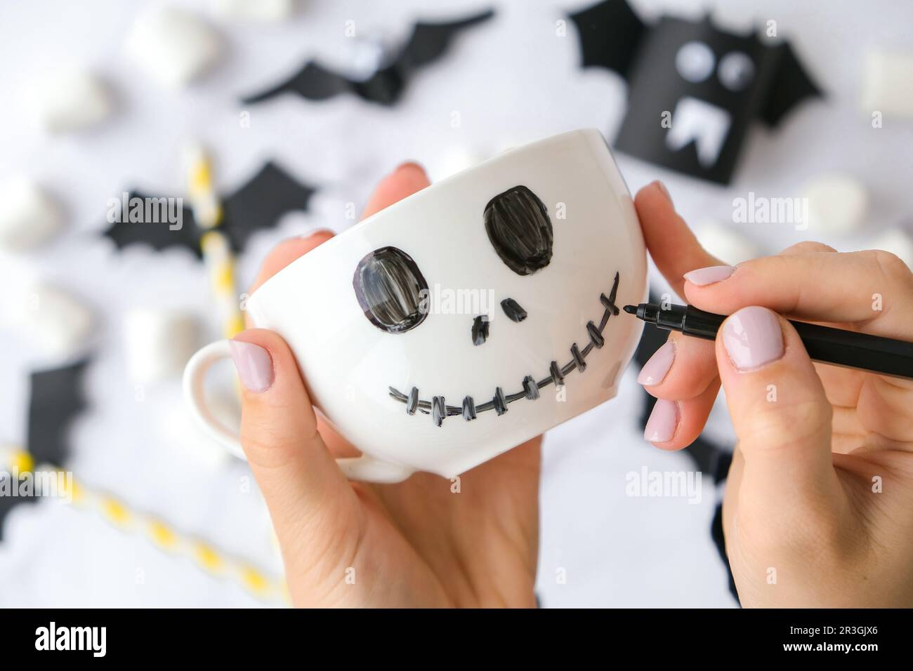 Female hands paint on white cup scary jacks face DIY for kids Halloween home activities Holiday art children craft Handmade deco Stock Photo