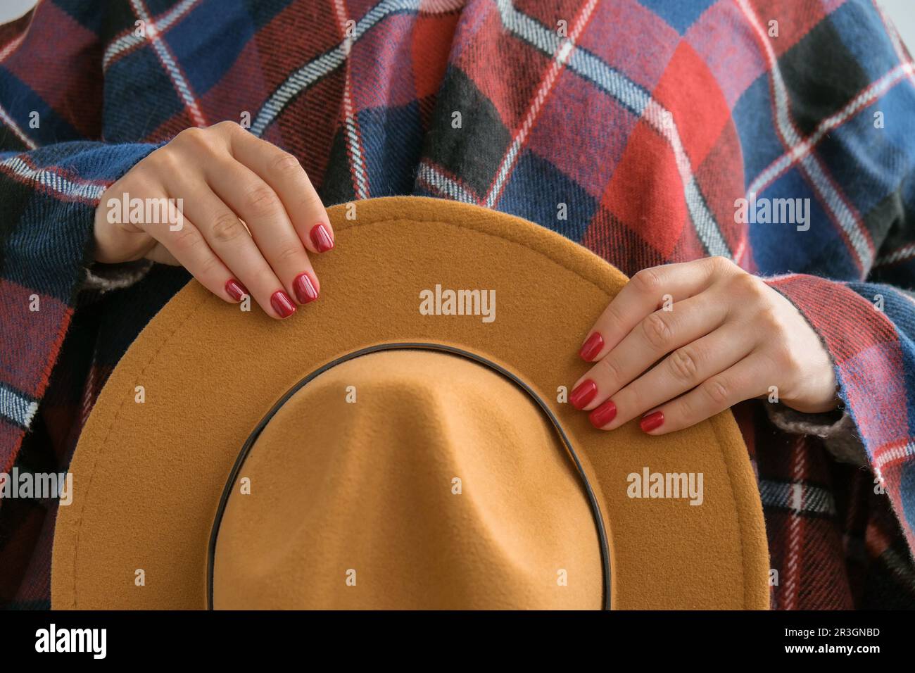 Stylish red female nails. Woman in poncho holding brown trendy hat. Modern Beautiful manicure. Autumn winter nail design concept Stock Photo