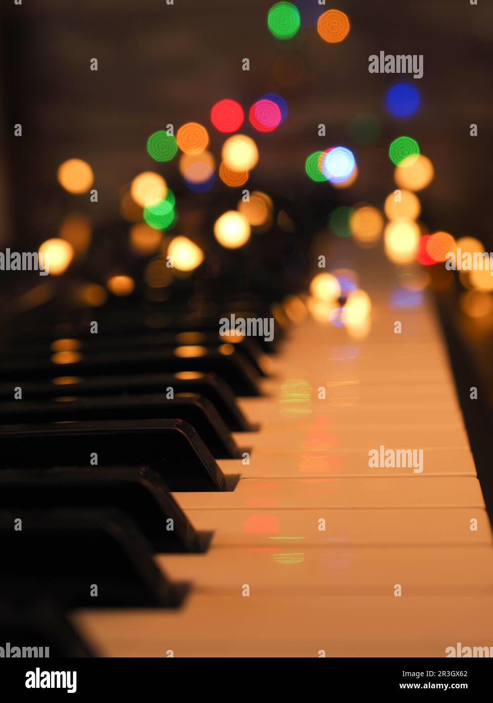 Piano keyboard with fairy lights and colorful blurred Christmas lights, seasonal background Stock Photo