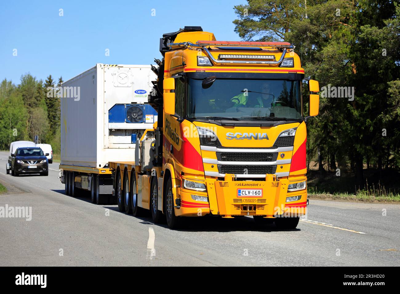 Yellow-red Scania R650 crane truck Pihala pulls trailer along highway 2 on a sunny day of spring in Forssa, Finland. May 19, 2023. Stock Photo