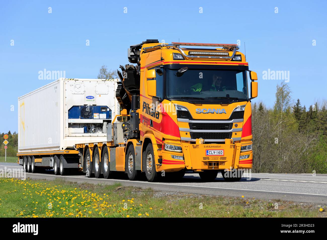 Yellow-red Scania R650 crane truck Pihala pulls trailer along highway 2 on a sunny day of spring in Forssa, Finland. May 19, 2023. Stock Photo