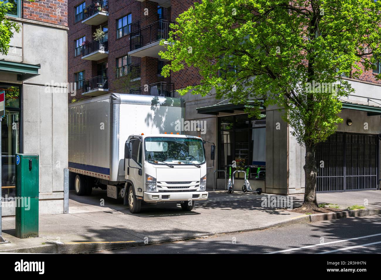 Industrial light duty transportation cab over powerful compact white rig semi truck with big box trailer standing on the urban city street making the Stock Photo