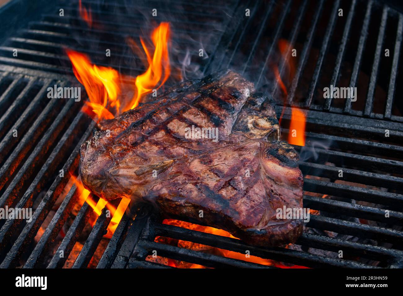 Barbecue dry aged wagyu porterhouse beef steak grilled as closeup on a charcoal grill with fire