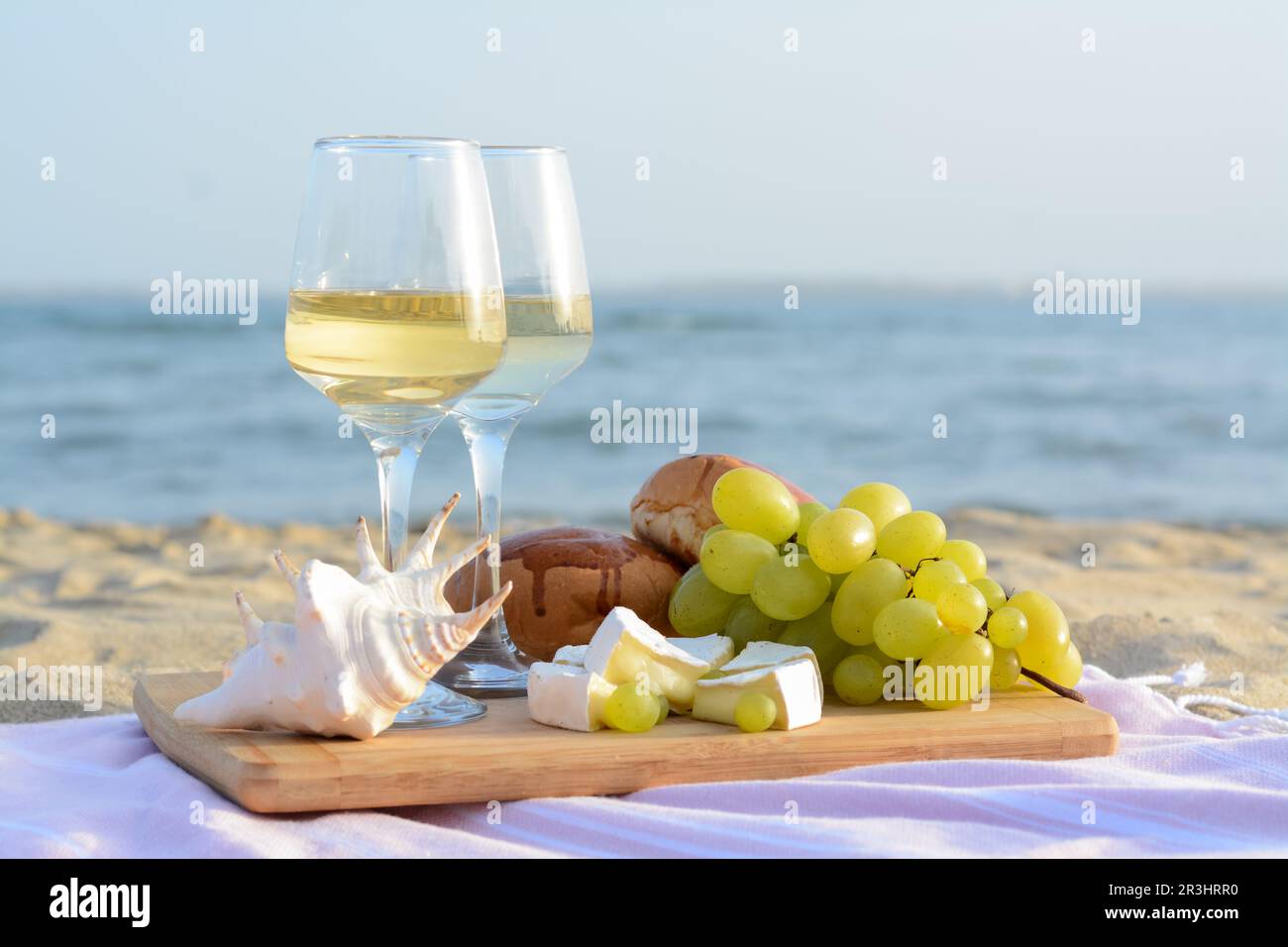 Glasses with white wine and snacks for beach picnic on sandy seashore ...