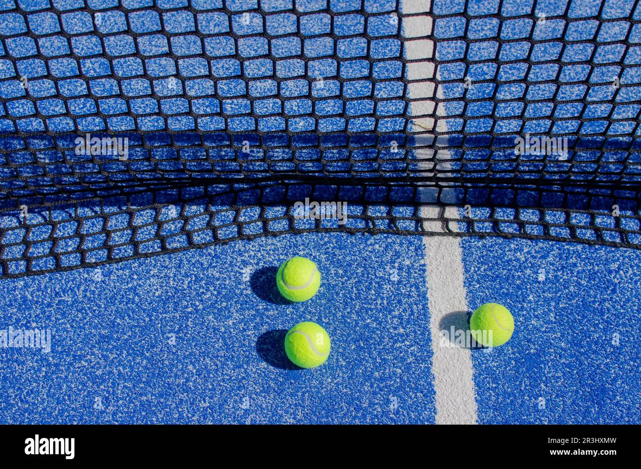 three balls near the net in a blue paddle tennis court, racket sports