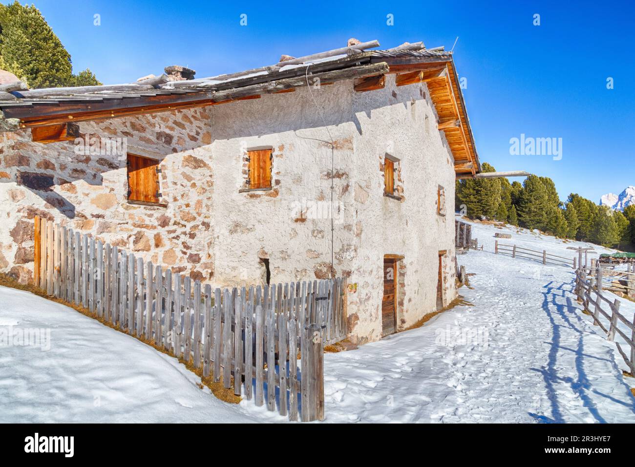High-altitude mountain hut among snow-capped peaks and pine forest Stock Photo