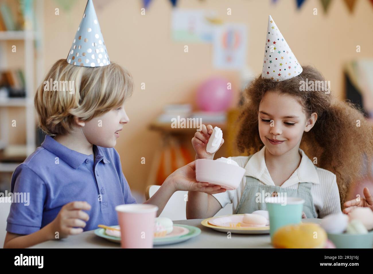 Portrait of two happy kids wearing party hats and enjoying sweets at ...