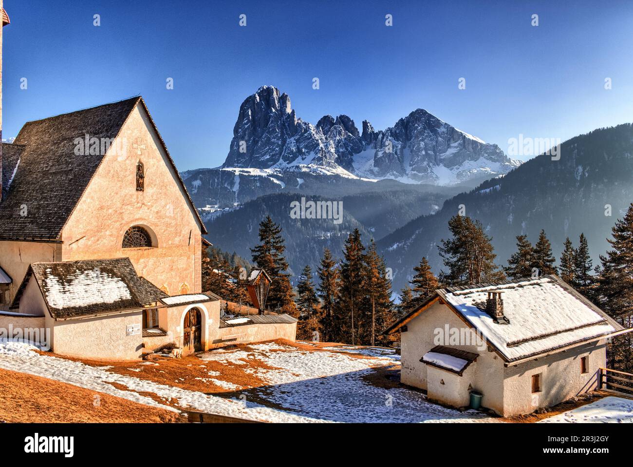 Church of St. Jacob overlooking pine forests and snow-capped peaks in winter Stock Photo