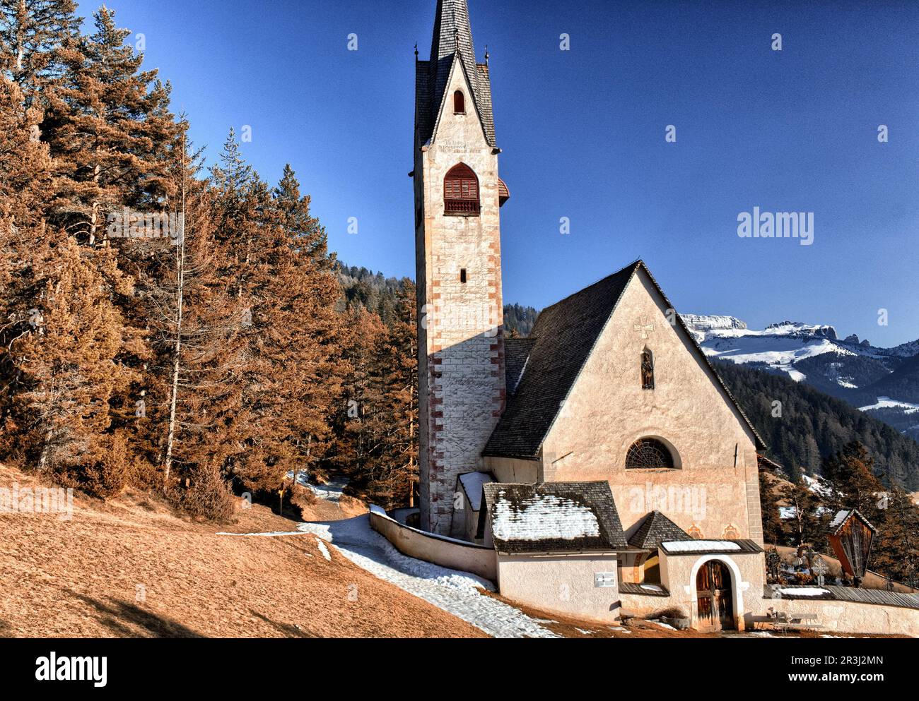 Church of St. Jacob overlooking pine forests and snow-capped peaks in winter Stock Photo