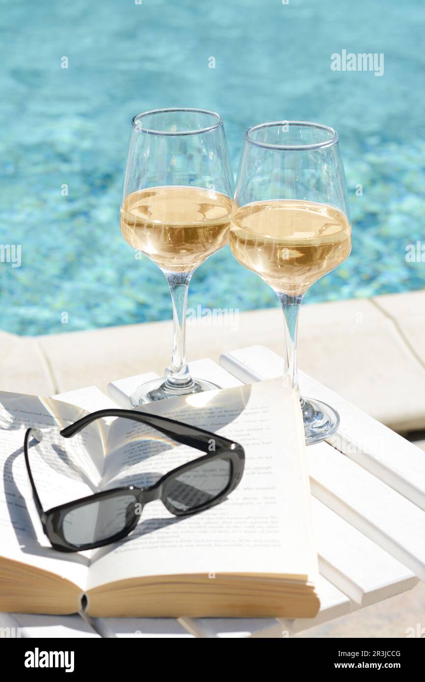 Glasses of tasty wine, sunglasses and open book on swimming pool edge Stock  Photo - Alamy