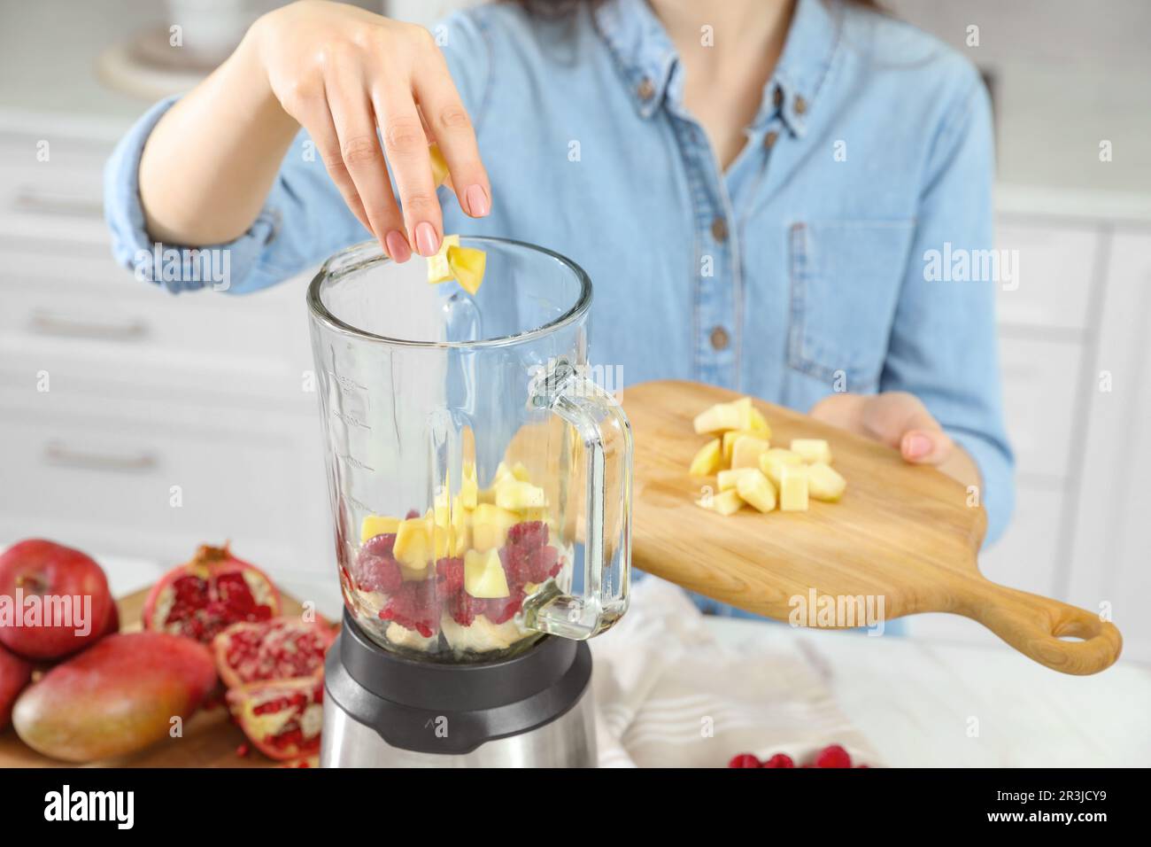 Woman adding mango into blender with ingredients for smoothie indoors